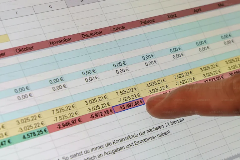 a hand pointing at a spreadsheet on a computer screen