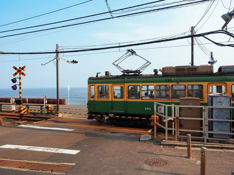 Railway crossing near Kamakurakokomae Station with the Enoden train and Pacific Ocean in the background