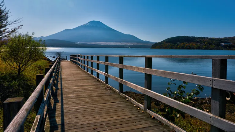 Wooden boardwalk leading toward Mount Fuji across calm Lake Yamanaka, Japan
