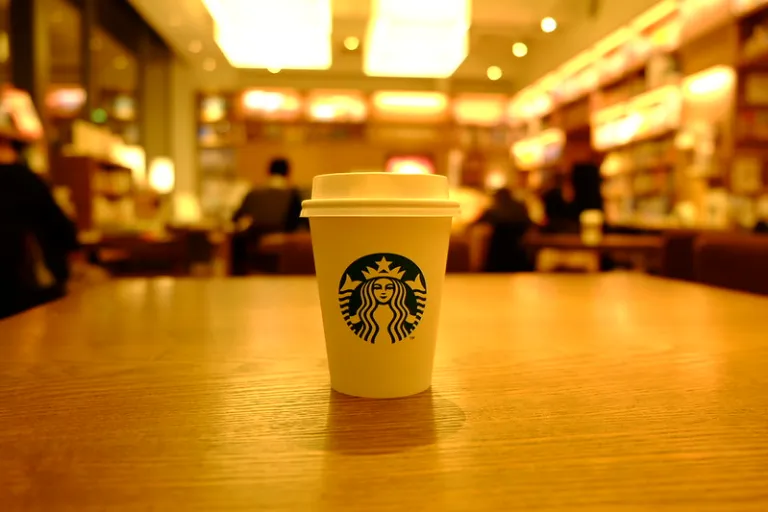 A cup of Starbucks coffee inside Daikanyama Tsutaya Books, with warm lighting and bookshelves in the background.