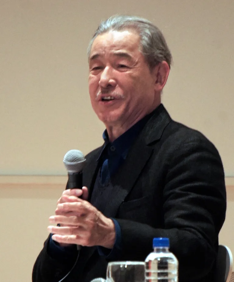 A portrait of Japanese fashion designer Issey Miyake speaking into a microphone during an event in Tokyo