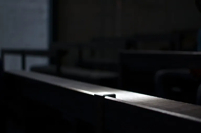 Close-up of a wooden pew inside the Church of the Light, illuminated by a narrow beam of natural light against a dark concrete interior.