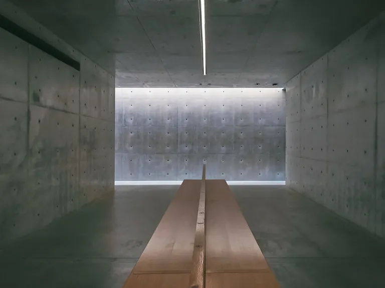 Interior of Chichu Art Museum, featuring exposed concrete walls, a long wooden bench, and soft natural light.