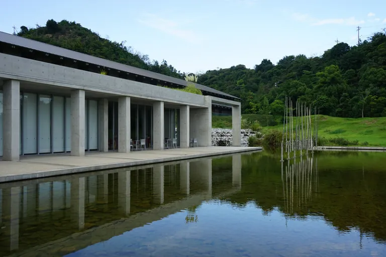 Exterior of Benesse House on Naoshima, designed by Tadao Ando with exposed concrete architecture reflected in a tranquil pond.