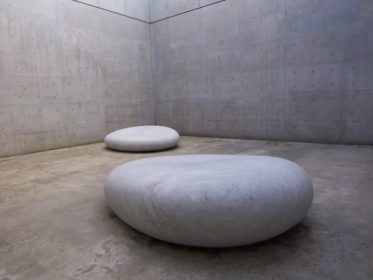 Minimalist interior of Benesse House, featuring smooth stone sculptures against Tadao Ando's exposed concrete walls.