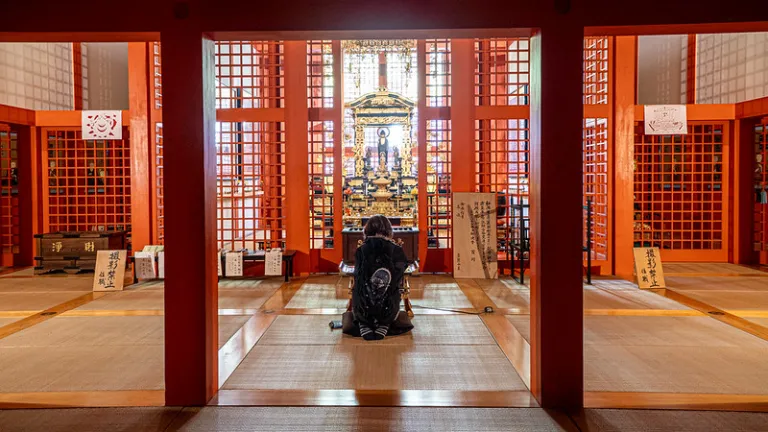 Visitor praying inside Honpukuji Water Temple, where Tadao Ando's minimalist architecture frames a vibrant vermilion interior.