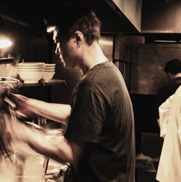 Chef preparing ramen in the open kitchen at YAKUMO in Tokyo.