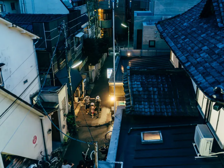 An evening view of Kosugiyu in Koenji, Tokyo, surrounded by narrow residential streets and tiled rooftops.