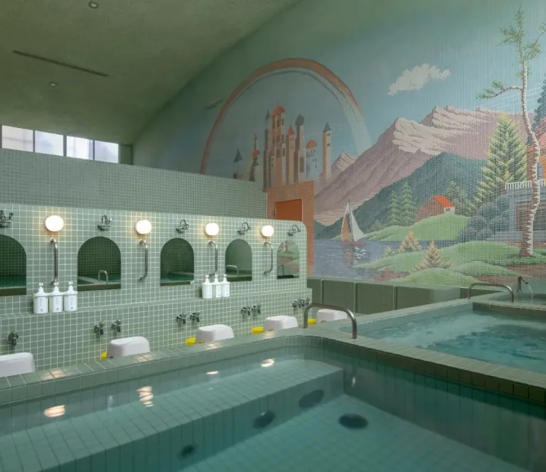 Interior of Koganeyu, featuring tiled baths, washing stations and a colourful mural above the bathing area.