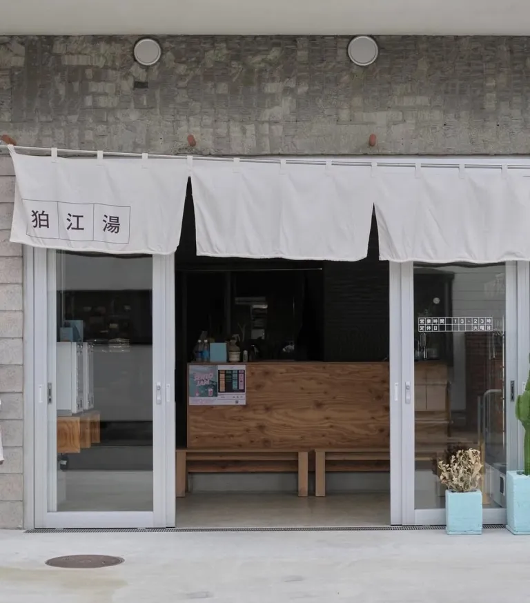 Exterior of Komaeyu, a renovated sento in Komae, Tokyo, with white noren curtains at the entrance.
