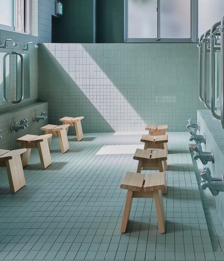 Washing area inside Komaeyu, featuring pale green tiles, wooden stools and soft natural light.