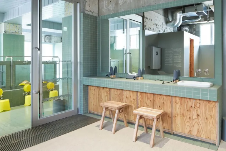 Vanity area inside Komaeyu, featuring pale green tiles, wooden counters and stools, and a bright modern interior.