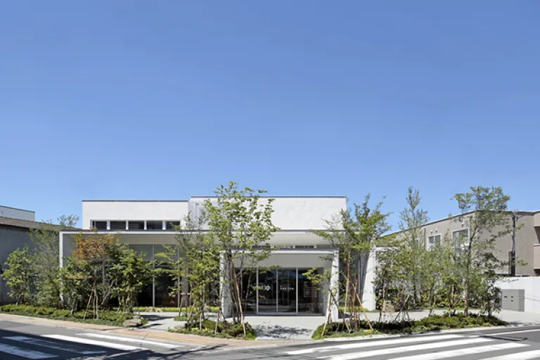 Exterior of Hisamatsuyu, a modern sento in Nerima, Tokyo, surrounded by trees under a clear blue sky.