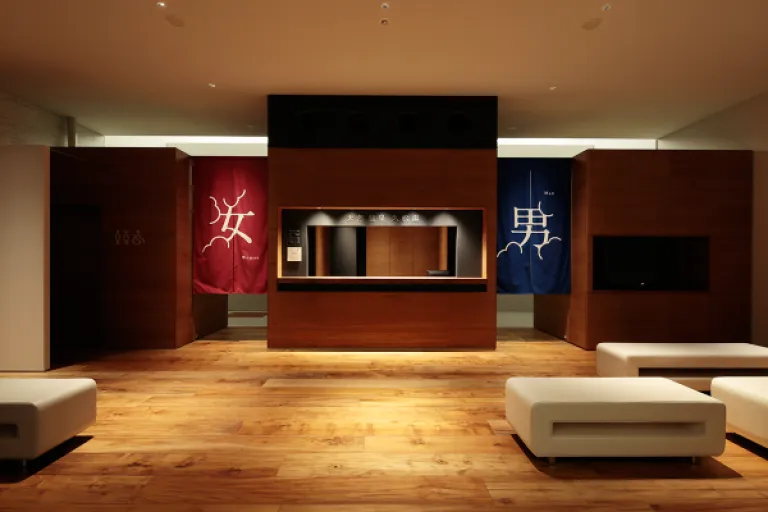 Reception area inside Hisamatsuyu, featuring warm wooden interiors, seating and red and blue noren curtains.