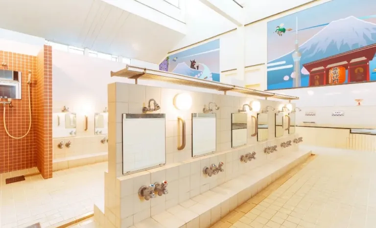 Bright bathing area inside Akebonoyu, featuring white tiled washing stations and colourful Mount Fuji murals on the walls.