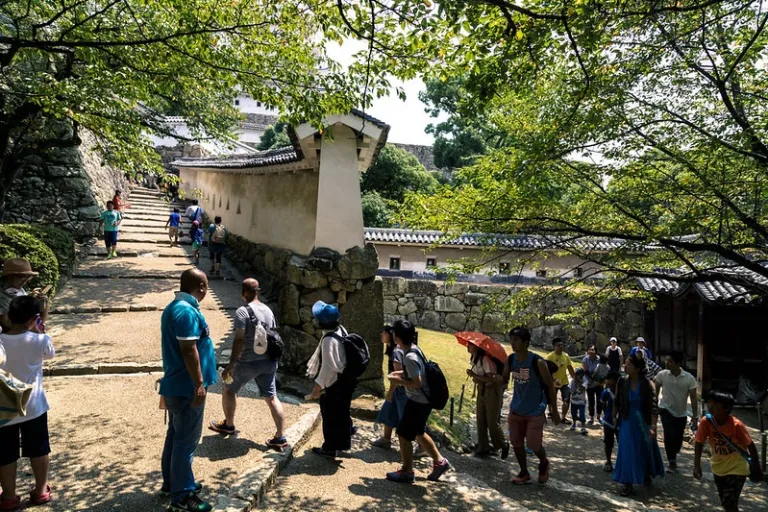 Visitors walking up a stone slope and pathways past traditional plaster walls and stone foundations at Himeji Castle