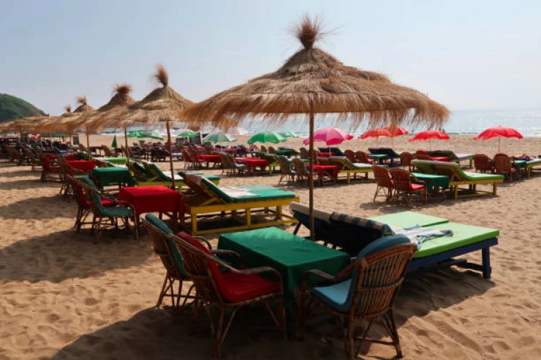 beach holiday with wooden green sun loungers beds under parasol umbrellas in a row, beach towels for sunbathing and sleeping outside in shade